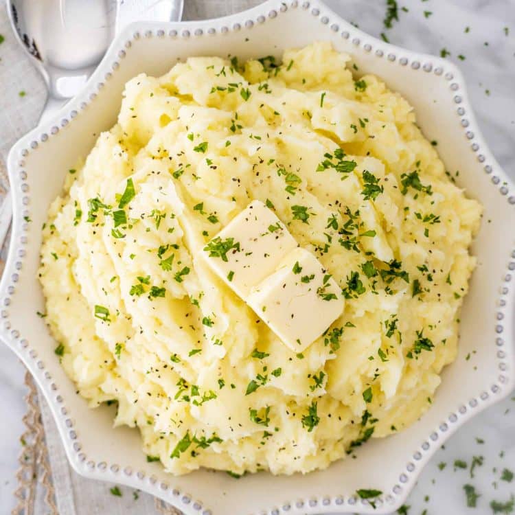 Fluffy Instant Pot mashed potatoes served in a white bowl, topped with melted butter and fresh parsley for a classic holiday side.