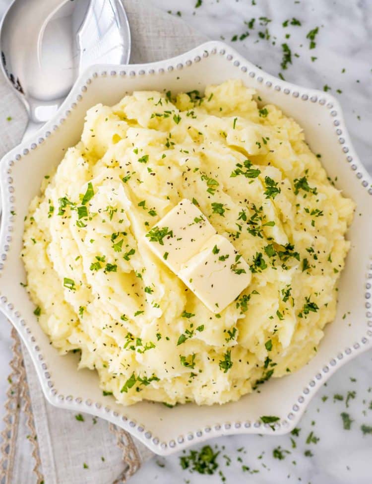 Fluffy Instant Pot mashed potatoes served in a white bowl, topped with melted butter and fresh parsley for a classic holiday side.
