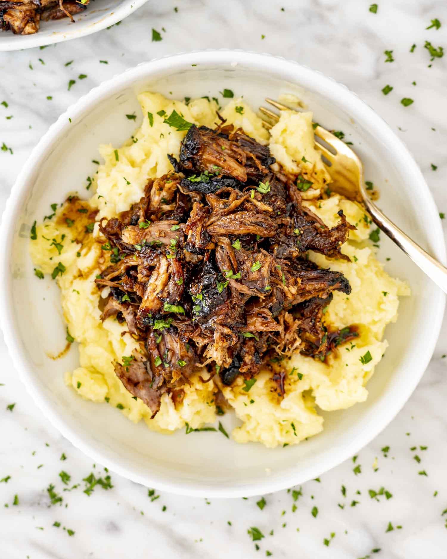 Tender Instant Pot mashed potatoes topped with juicy brown sugar balsamic pulled pork, served in a white bowl with parsley garnish.