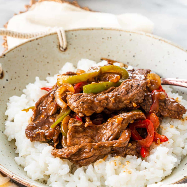 pepper steak over a bed of rice in a bowl