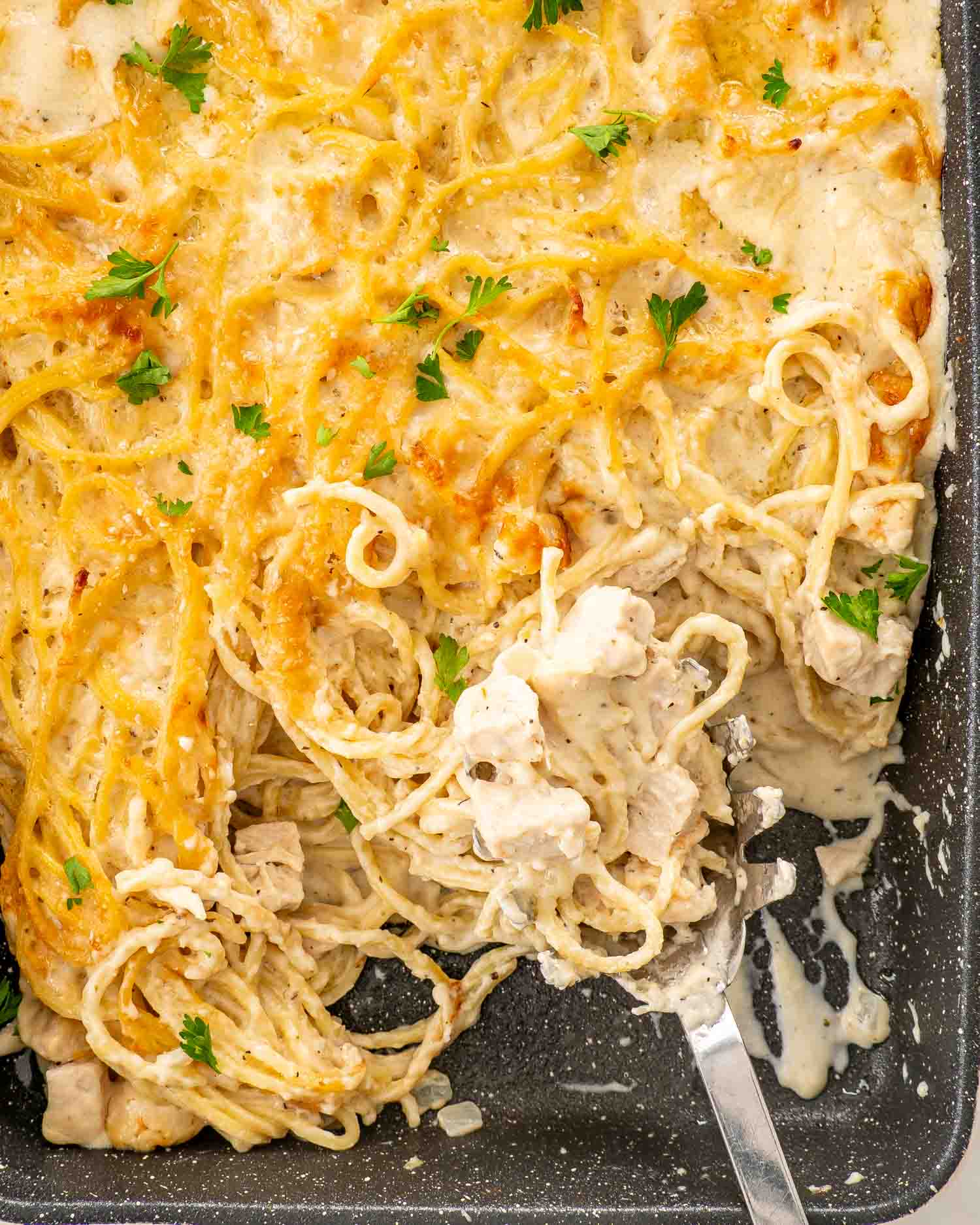 Overhead close-up of partially served turkey tetrazzini with golden spaghetti, creamy sauce, turkey chunks, and parsley in a baking dish.