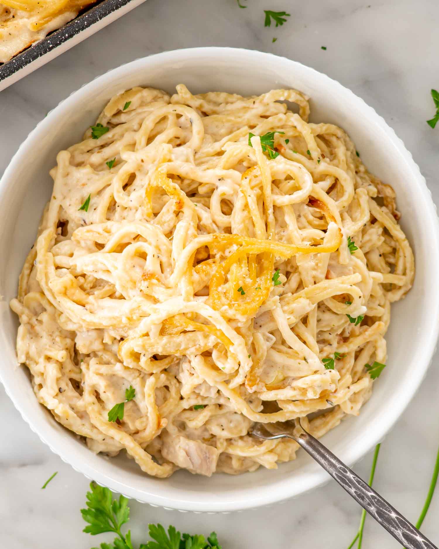 Overhead view of creamy turkey tetrazzini in a white bowl, with golden spaghetti strands, turkey pieces, parsley, and a fork.
