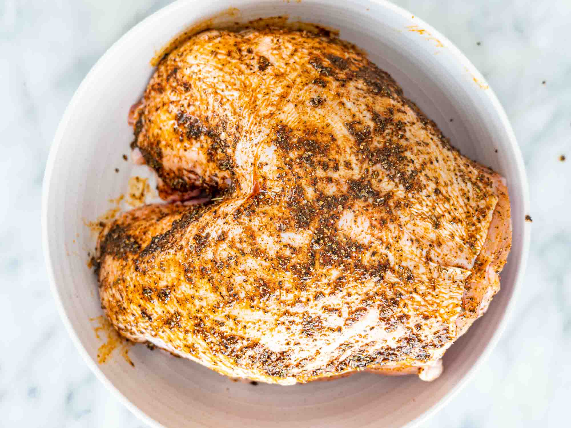 an uncooked turkey breast with seasoning on it in a plate.