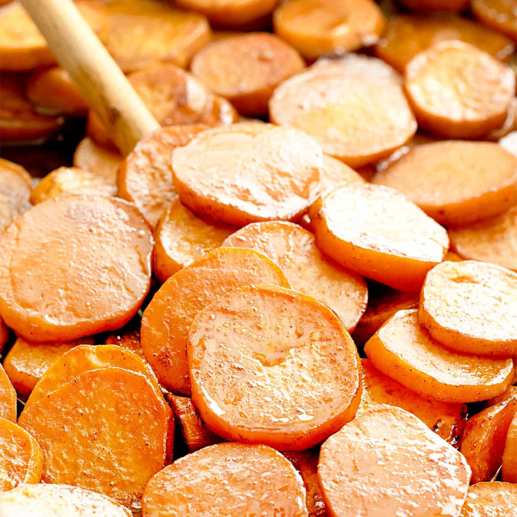 candied yams on a baking sheet with a wooden spoon inside.