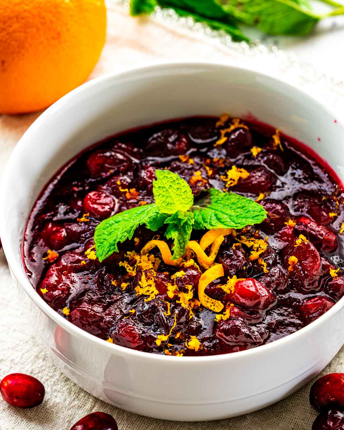 cranberry sauce in a white bowl with orange zest and a piece of mint.