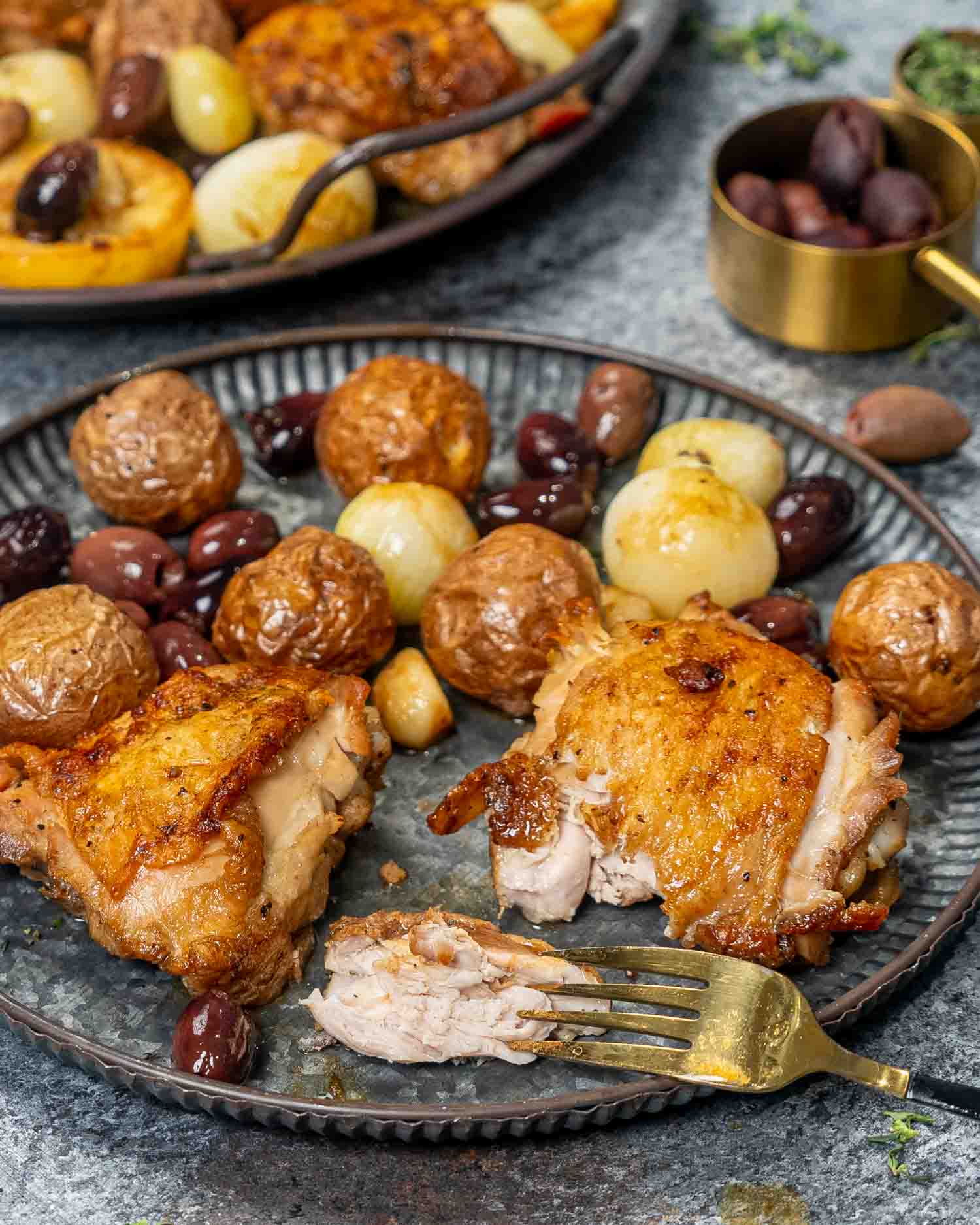 a serving of greek chicken thighs with some roasted potatoes on a metal plate.