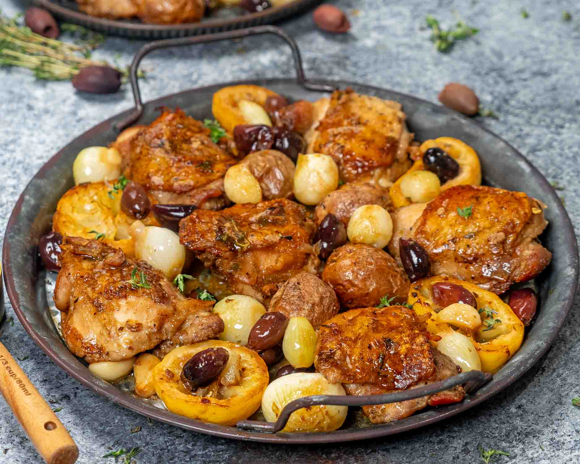 greek chicken thighs in a metal platter garnished with fresh thyme.