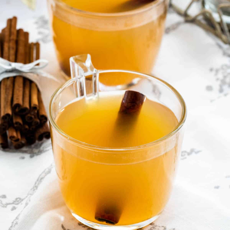 two mugs of hot mulled cider with cinnamon sticks in them