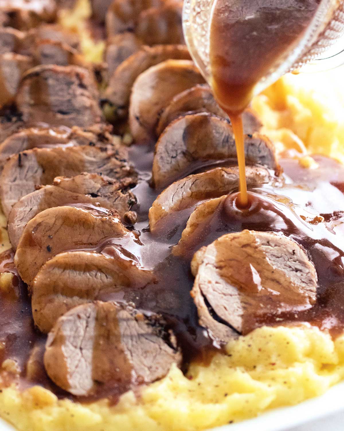 gravy being poured over sliced pork loin on top of a bed of mashed potatoes