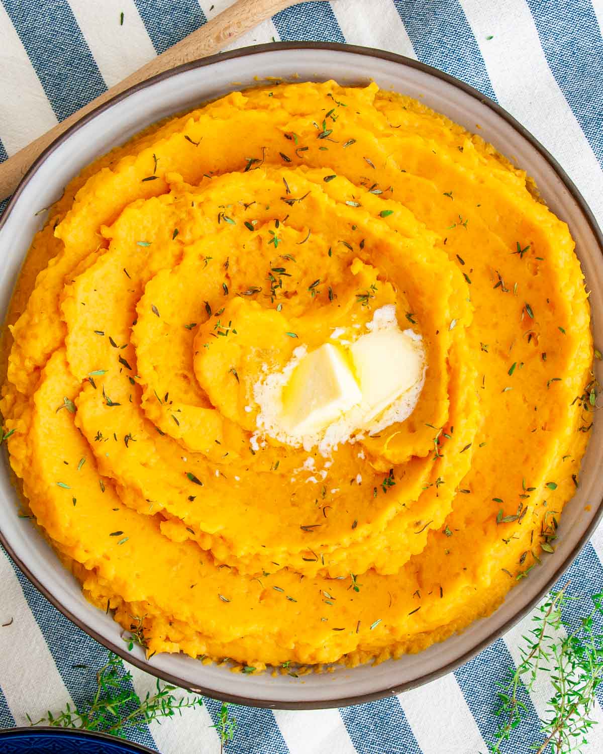 overhead shot of mashed sweet potatoes in a blue bowl with a couple pats of butter.