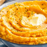 mashed sweet potatoes in a blue bowl with a couple pats of butter.