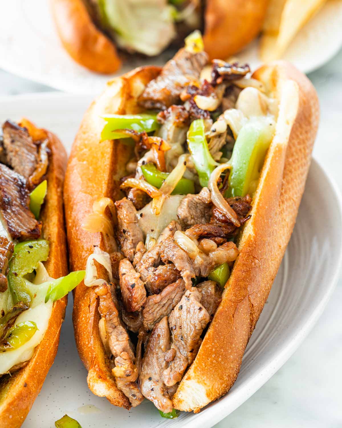 closeup of a philly cheesesteak sandwich on a white plate.