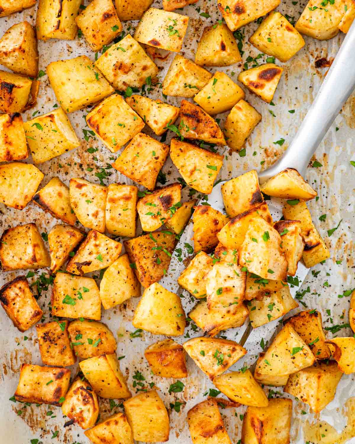 overhead shot of roasted sweet potatoes on a baking sheet with a spatula lifting some up.