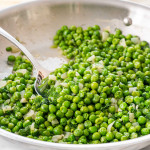 sautéed peas in a skillet with a serving spoon inside.