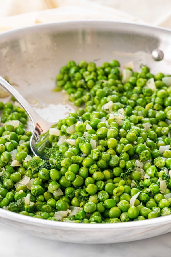 sautéed peas in a skillet with a serving spoon inside.