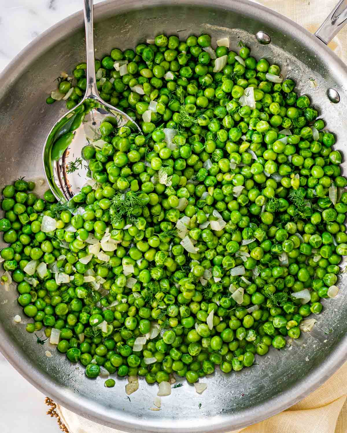 sautéed peas in a skillet with a serving spoon inside.