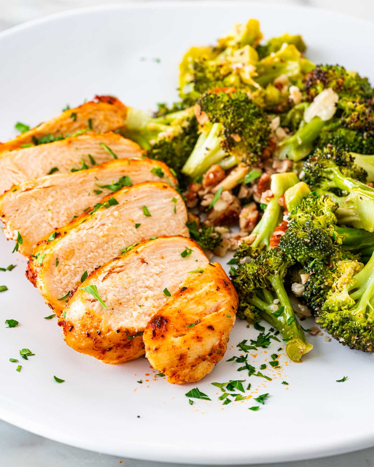a sliced chicken breast next to roasted broccoli on a white plate.