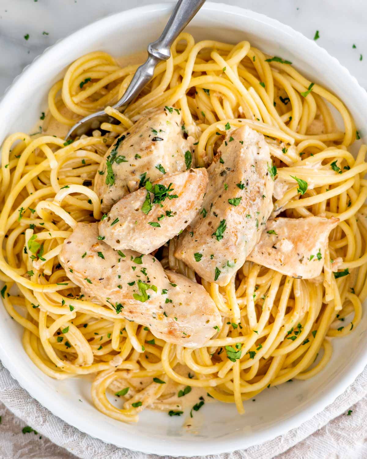 chicken lazone over a bed of spaghetti garnished with parsley.