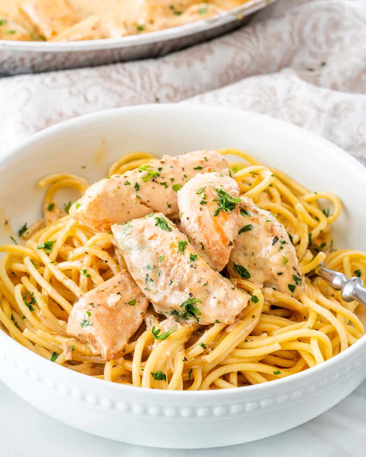 chicken lazone over a bed of spaghetti garnished with parsley.
