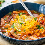 a blue bowl filled with chicken tortilla soup garnished with tortilla chips and cheese.