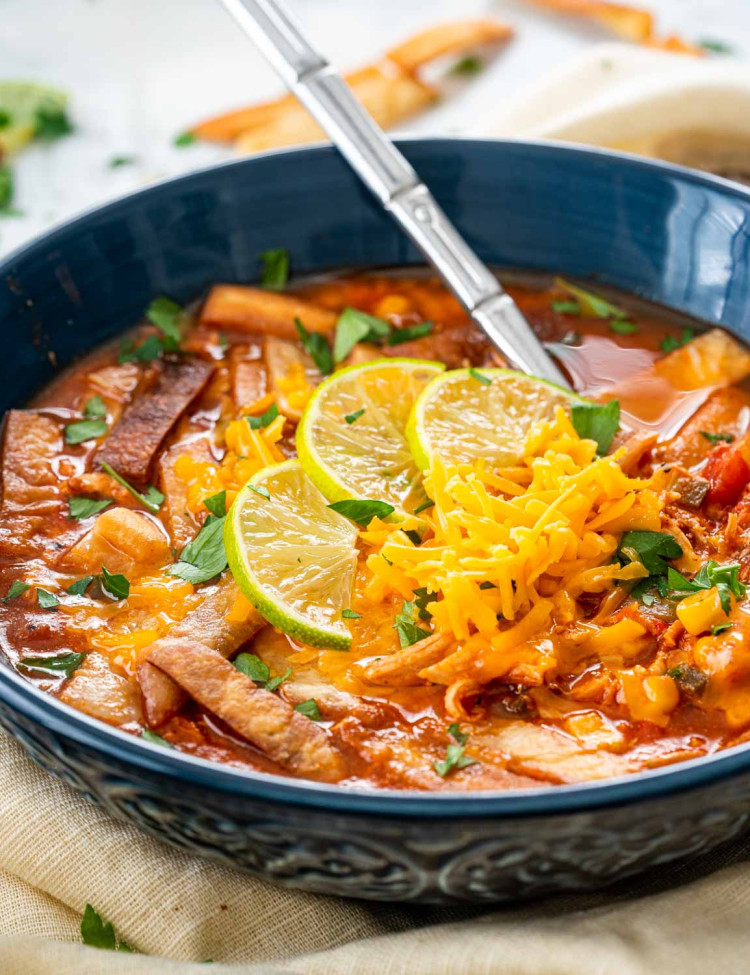 a blue bowl filled with chicken tortilla soup garnished with tortilla chips and cheese.