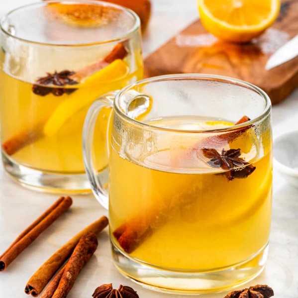 two mugs with hot toddy in them garnished with a cinnamon stick and lemon slice.