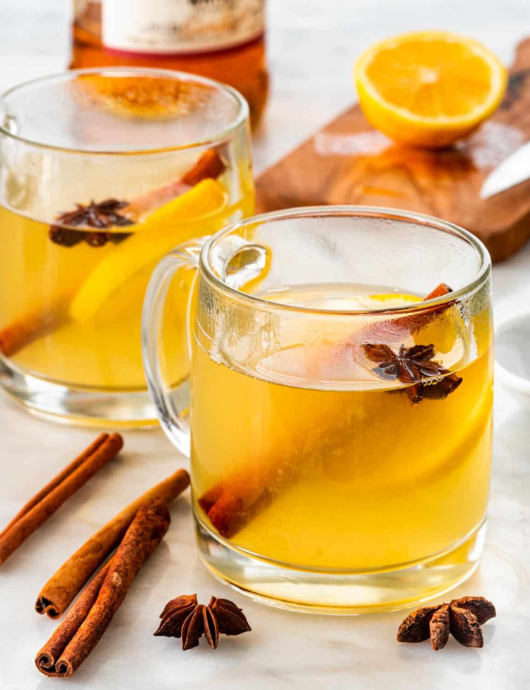 two mugs with hot toddy in them garnished with a cinnamon stick and lemon slice.