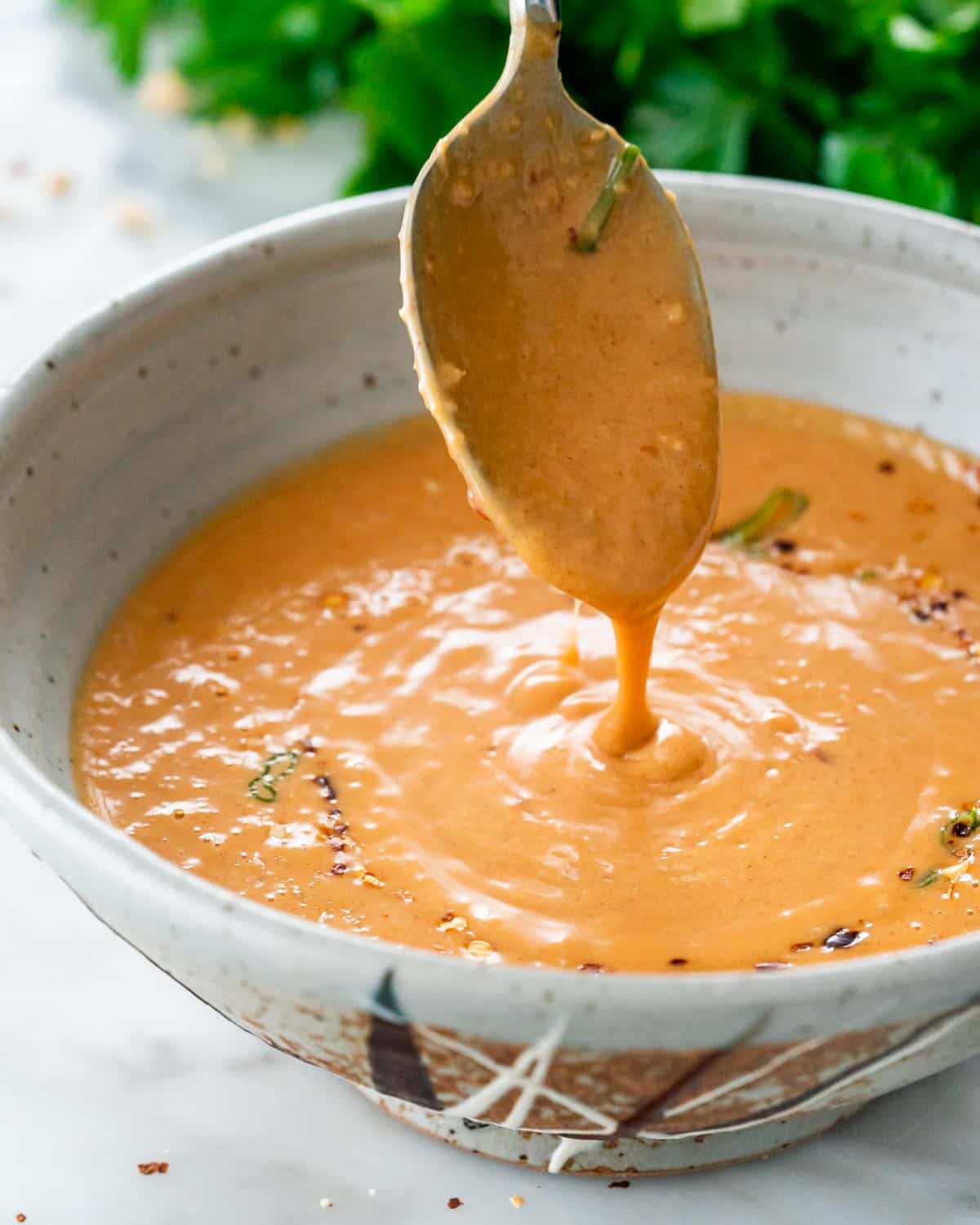 a spoon pouring some peanut sauce in a bowl.