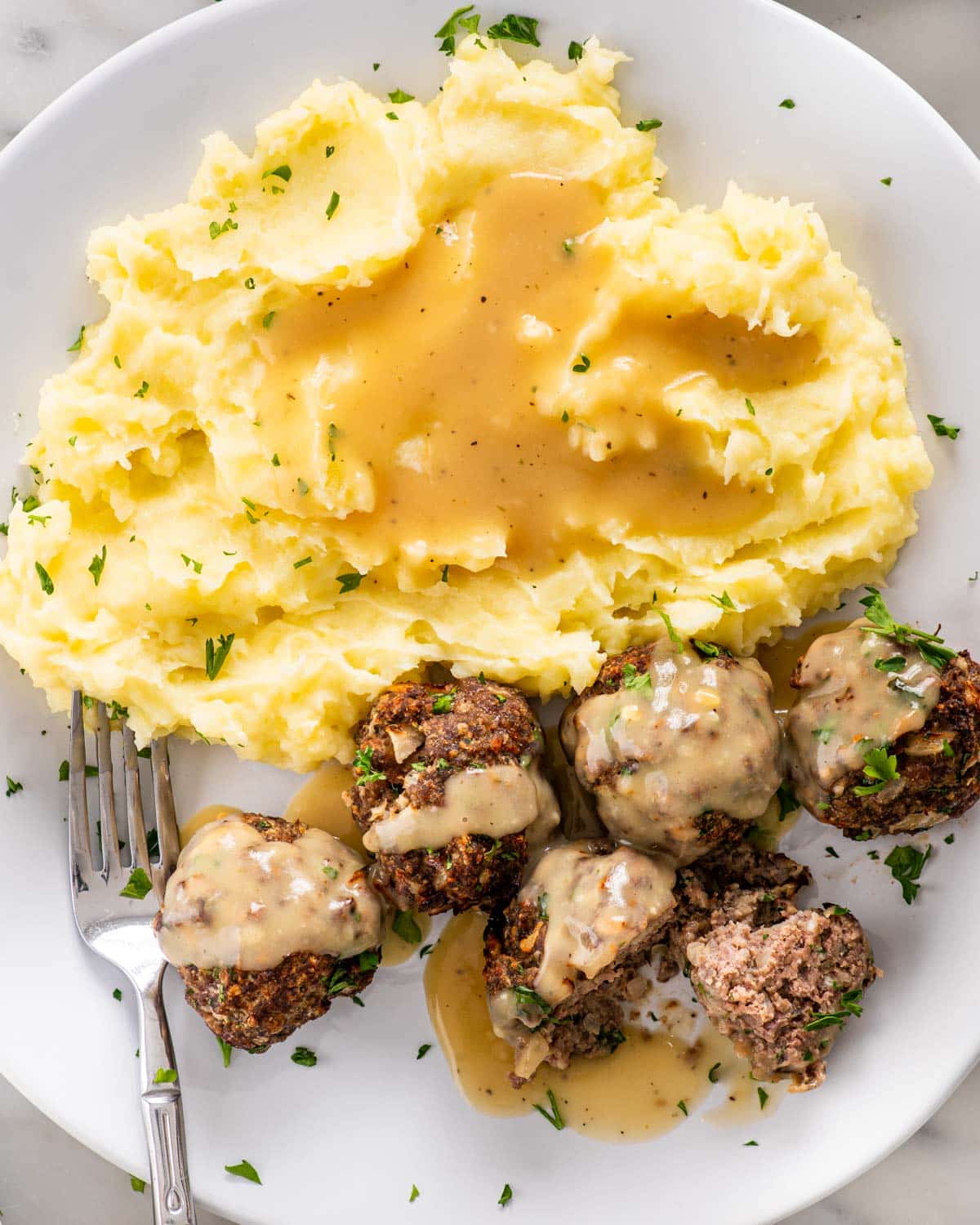 overhead shot of meatballs with mashed potatoes and gravy on a plate.