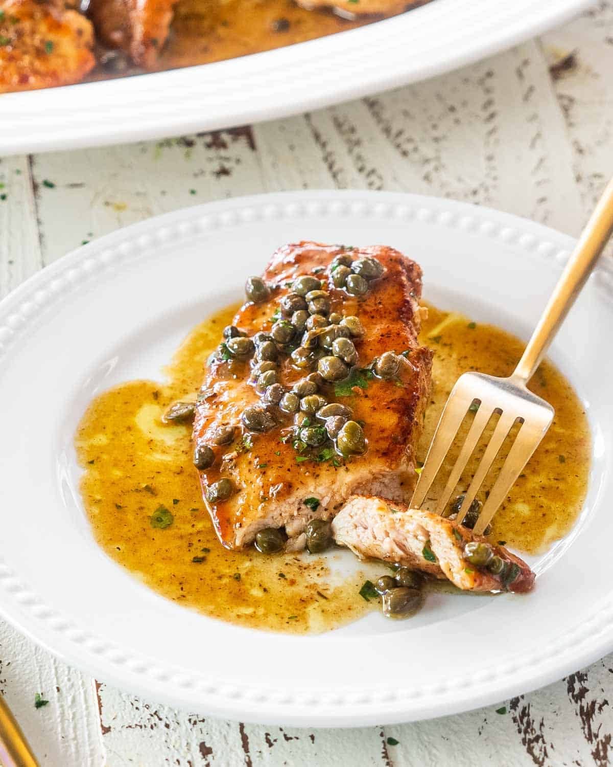chicken piccata on a white plate with a fork holding a piece.