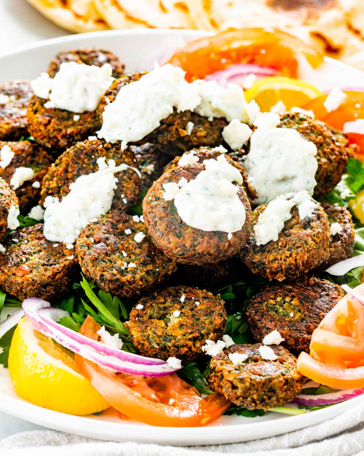 closeup of falafel on a plate with tzatziki, feta, tomatoes and onions.