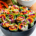 spring rolls cut in half in a black bowl with peanut sauce.