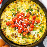 freshly baked frittata in a black skillet garnished with roasted tomatoes.