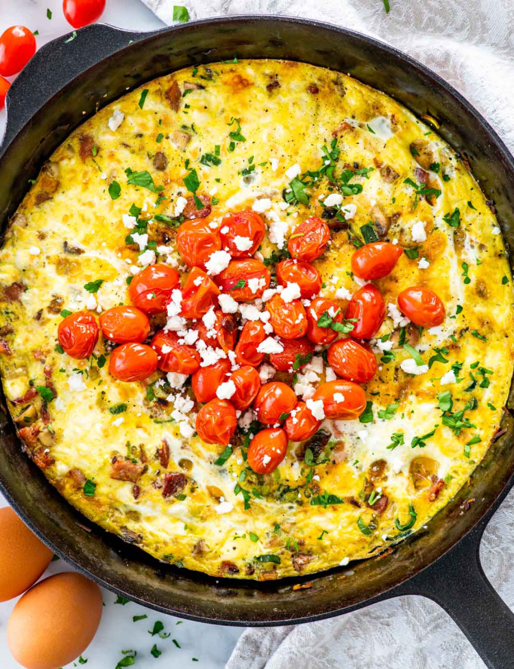 freshly baked frittata in a black skillet garnished with roasted tomatoes.