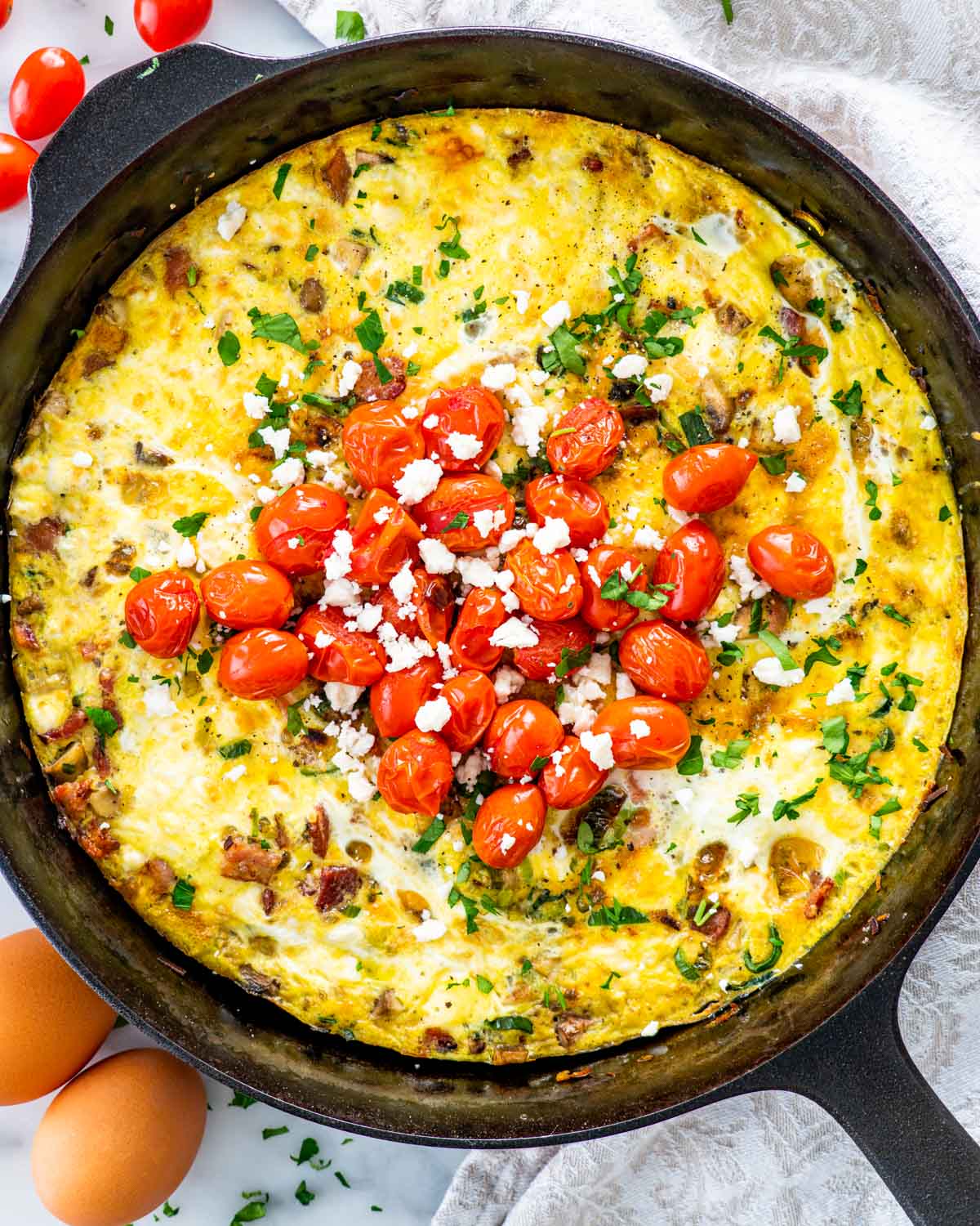 freshly baked frittata in a black skillet garnished with roasted tomatoes.
