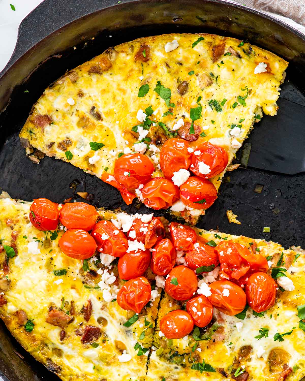 frittata cut into portions in a skillet garnished with roasted tomatoes.