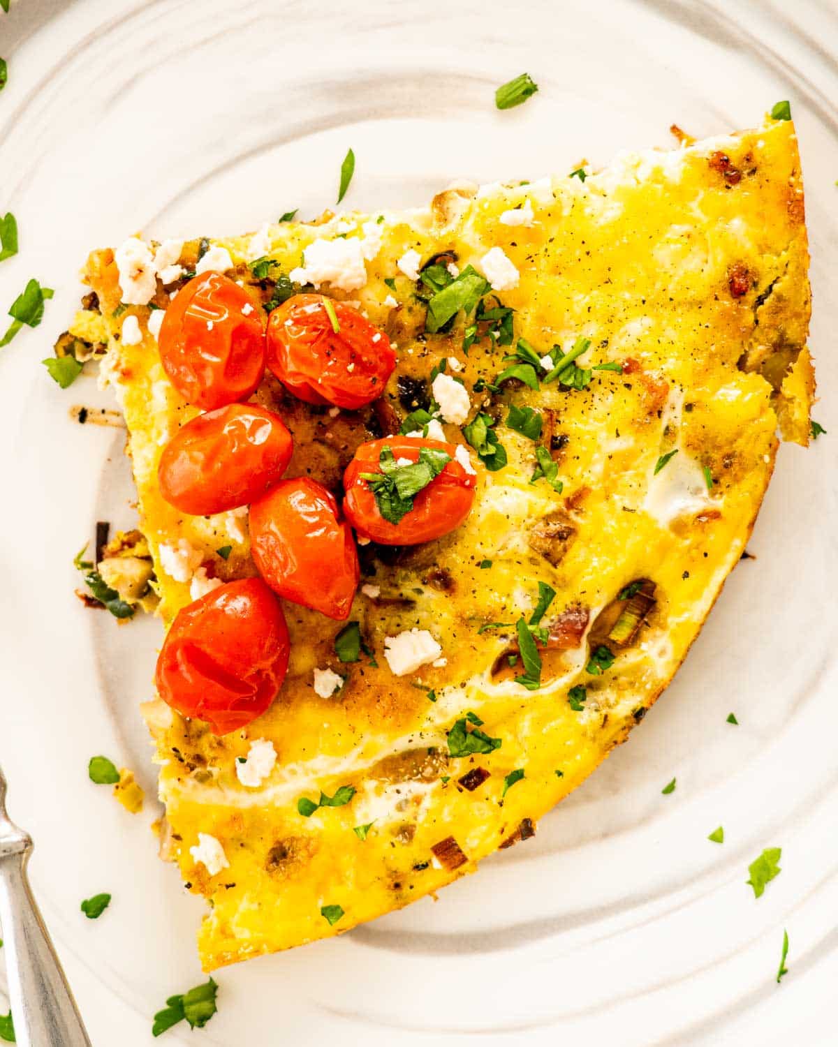 a slice of frittata garnished with roasted tomatoes on a white plate.