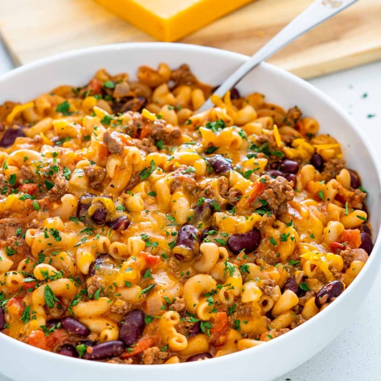 a large white bowl with freshly cooked chili mac with a serving spoon inside.