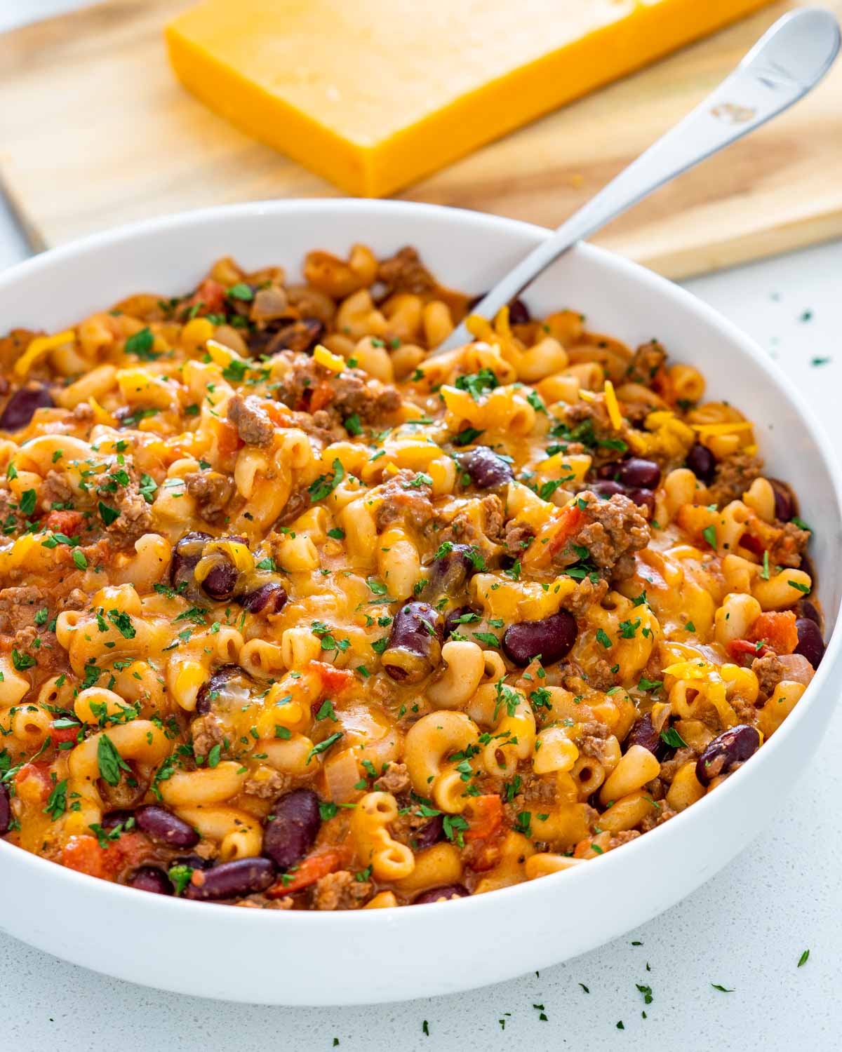 a large white bowl with freshly cooked chili mac with a serving spoon inside.