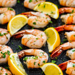 oven baked shrimp in a casserole dish with lemon wedges.