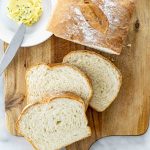overhead shot of freshly made potato bread on a cutting board with 3 slices a plate with a pat of butter.