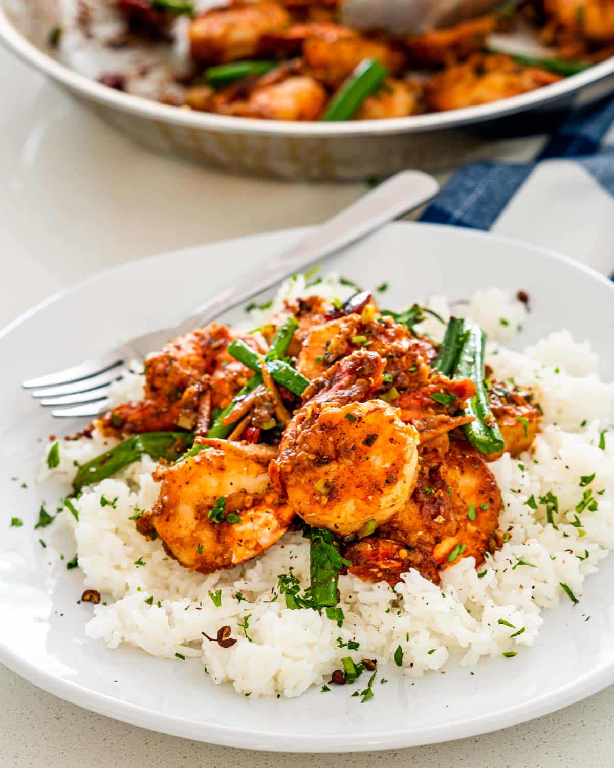 szechuan chili shrimp over a bed of rice on a white plate.