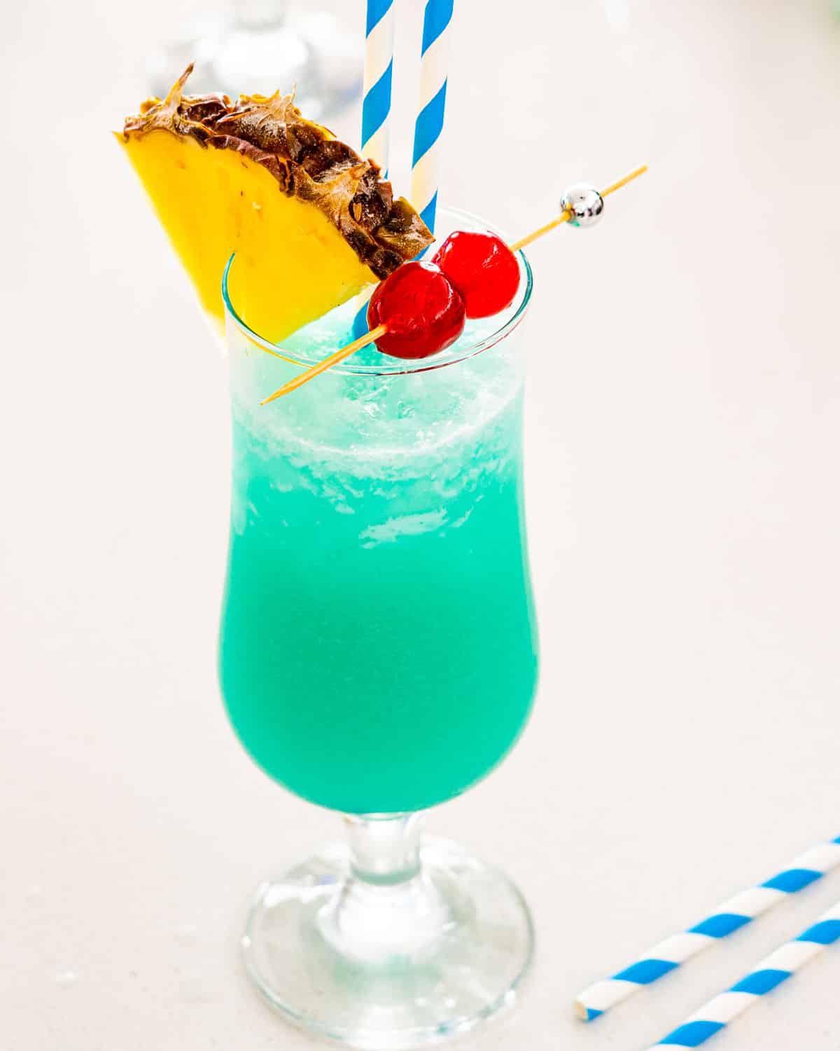 blue hawaiian in a glass garnished with pineapple and maraschino cherries.