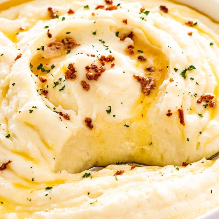 brown butter mashed potatoes in a big white bowl with a serving spoon inside.