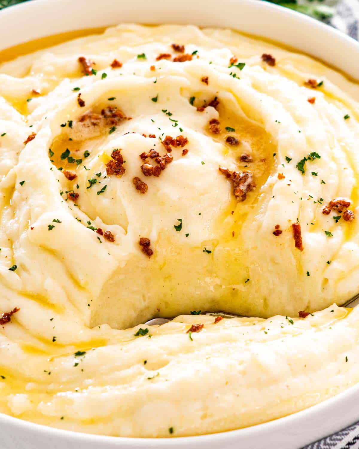 brown butter mashed potatoes in a big white bowl with a serving spoon inside.