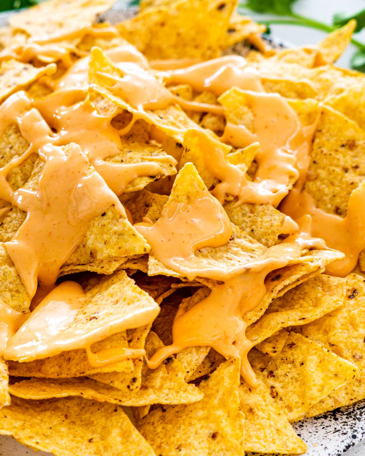 a plate full of tortilla chips drizzled with nacho cheese sauce.