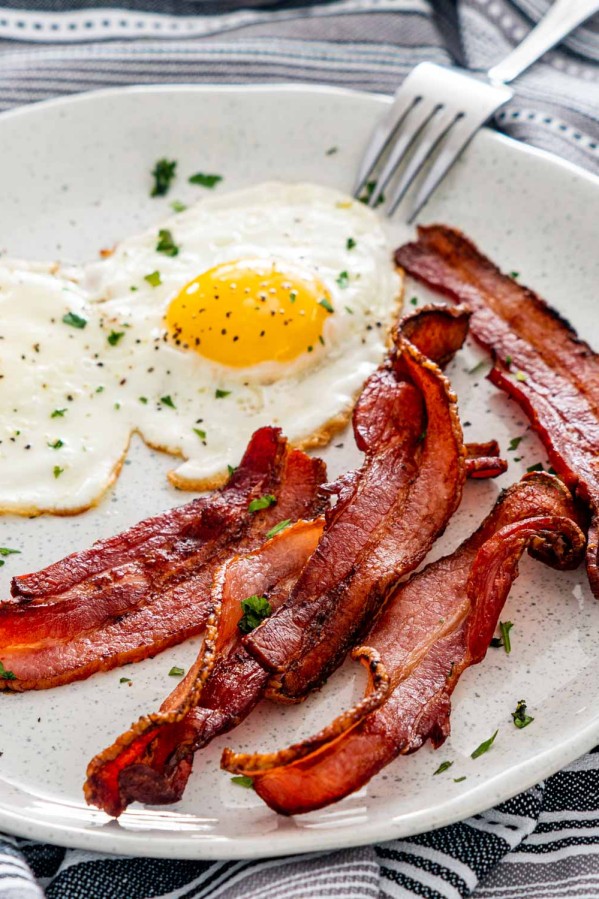 bacon made in the air fryer on a white plate with 2 sunny side up eggs.