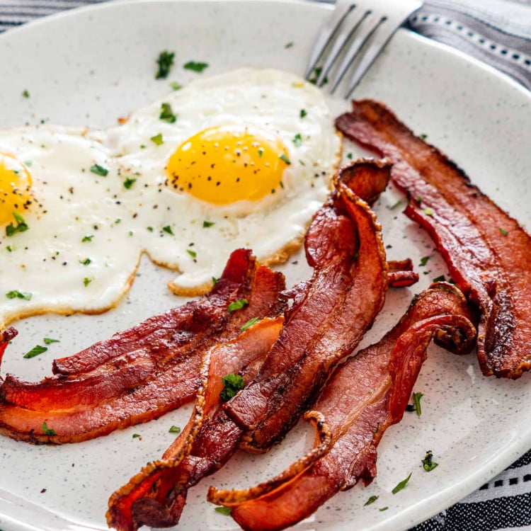 bacon made in the air fryer on a white plate with 2 sunny side up eggs.
