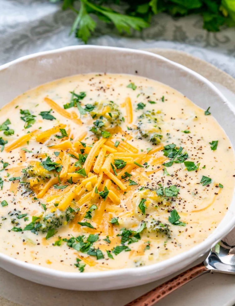 broccoli cheddar soup in a white bowl topped with more cheddar cheese and parsley.