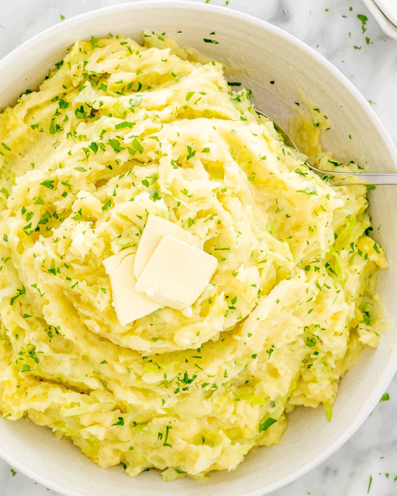 a big white bowl full of colcannon topped with butter.